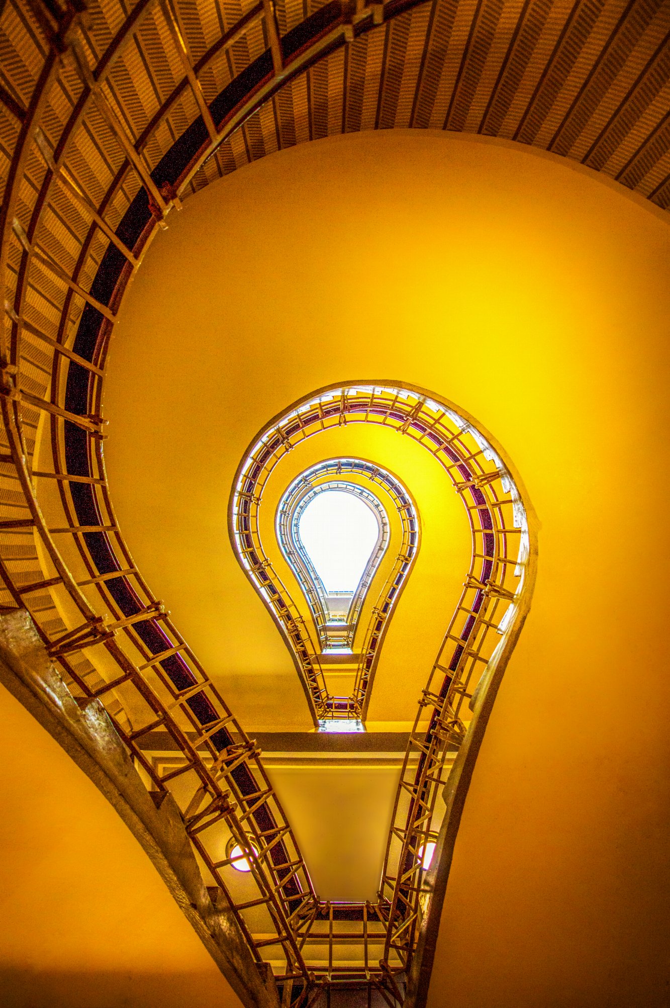 Escalier en spirale jaune photographié d’en bas, dont la forme évoque une ampoule, avec une lumière blanche au centre