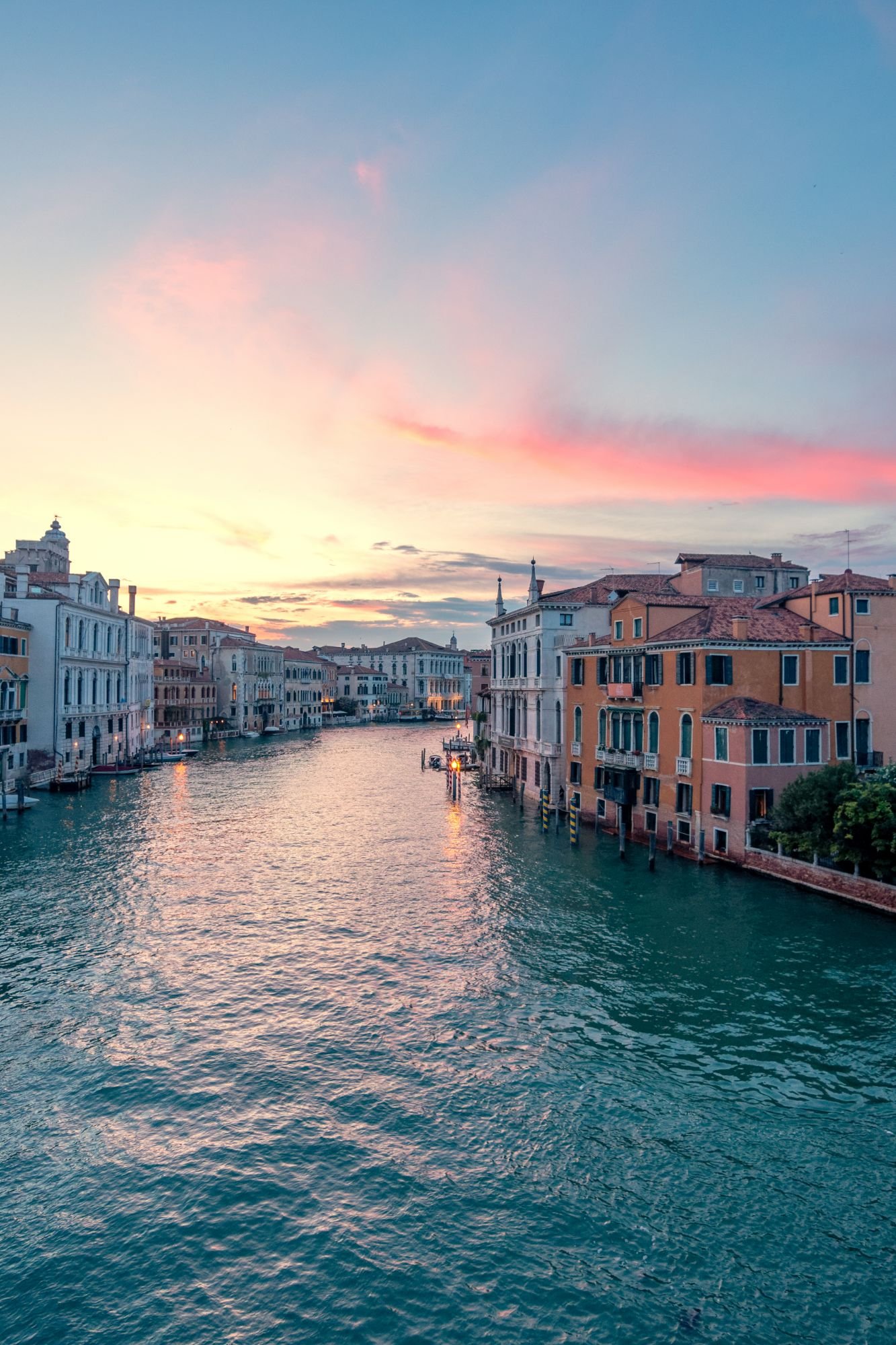 Le Grand Canal de Venise au coucher du soleil, palais aux façades ocre et ciel rose et bleu qui se reflète sur l’eau