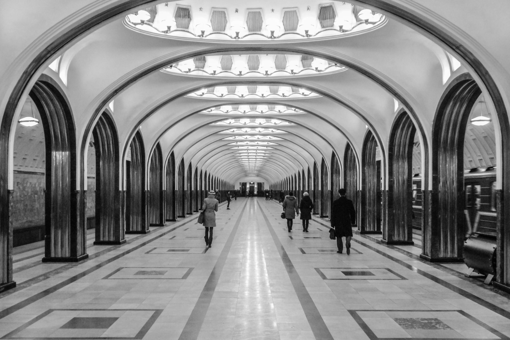 Station de métro monumentale en noir et blanc, succession d’arches et passants